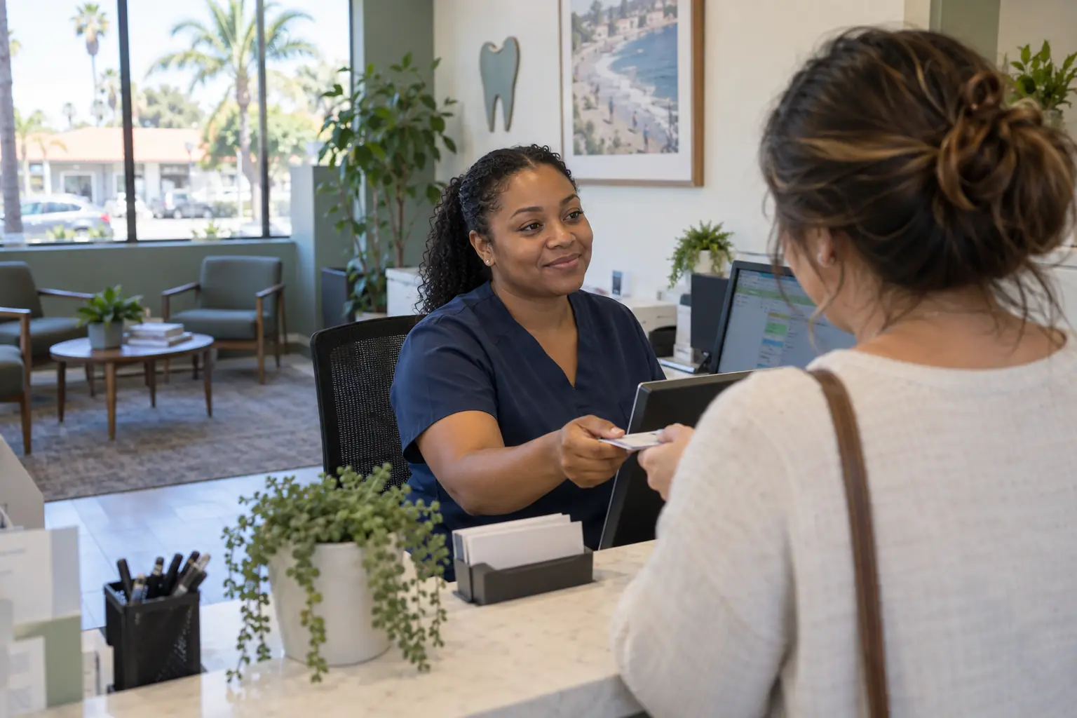 A smiling dental office coordinator checking in a patient at the front desk
