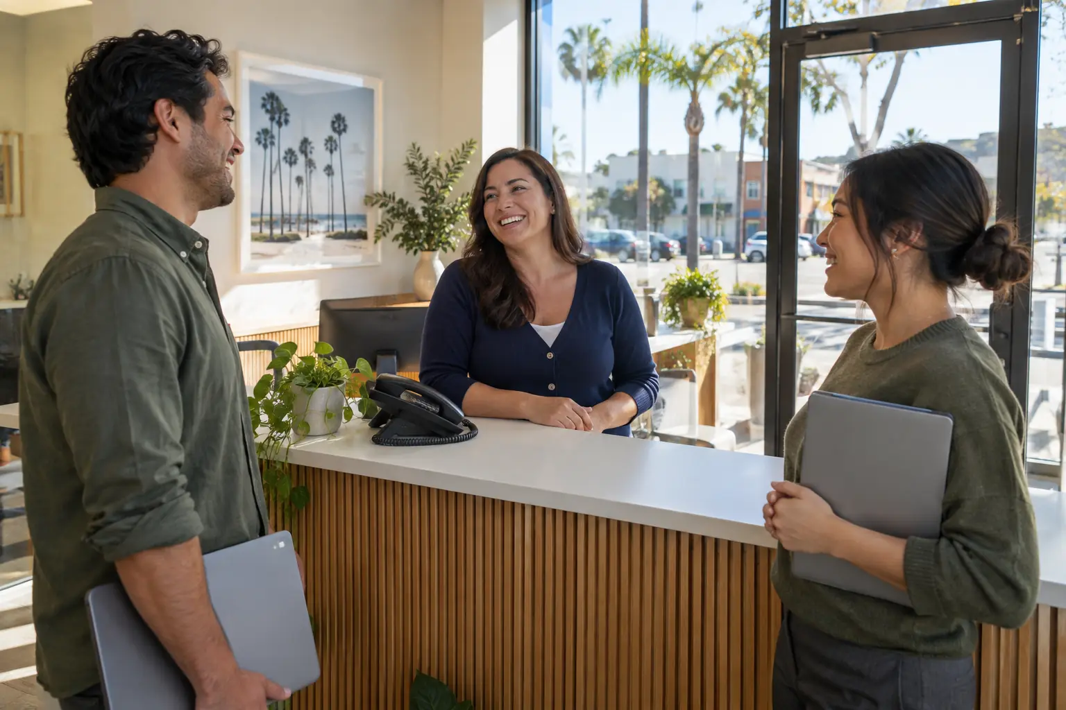 An office manager laughing with two coworkers at a bright front desk on a sunny morning