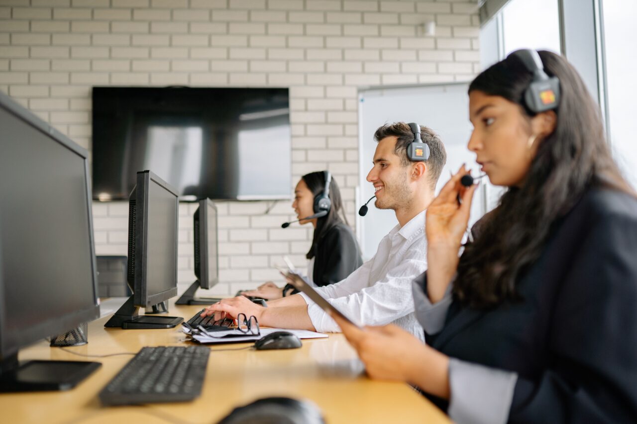 Three employees wearing headsets working at computer monitors in a modern office, providing support and collaborating