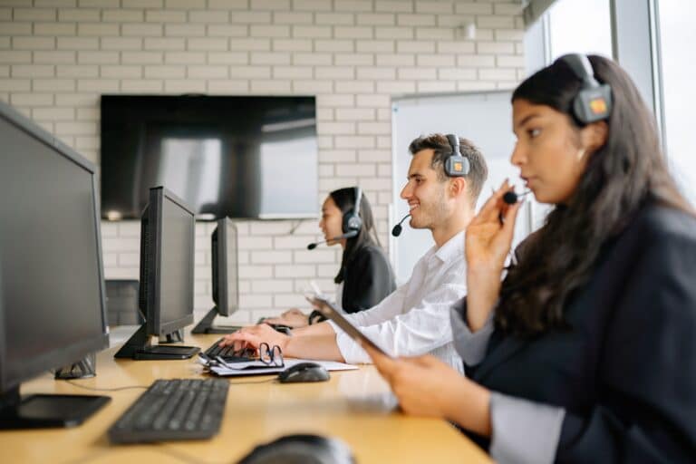 Three employees wearing headsets working at computer monitors in a modern office, providing support and collaborating